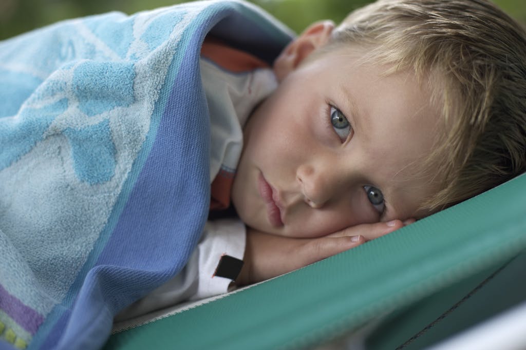 A young child lies under a blue blanket with a calm expression, evoking peace and innocence.