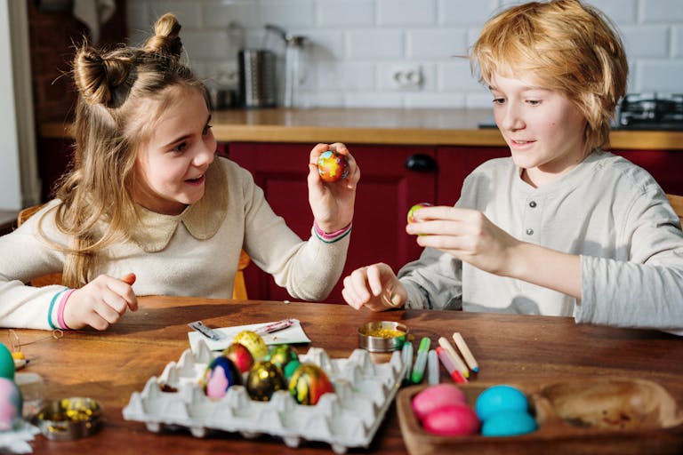 Two children enjoy decorating colorful Easter eggs indoors with creativity and fun.
