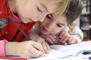 Two young girls focus on a drawing project together, sharing creativity and learning.
