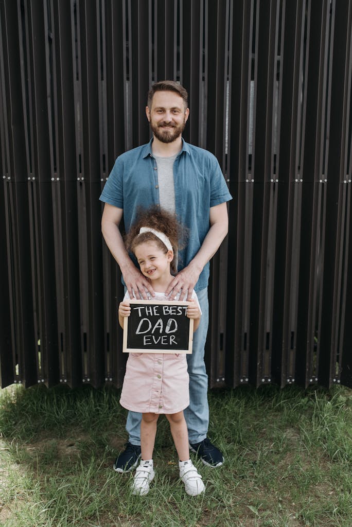 A joyful father and daughter sharing a bonding moment with a touching handwritten sign outdoors.