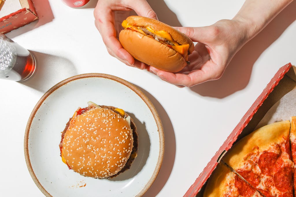 Cheeseburger with sesame seed bun and pepperoni pizza on a table, perfect for a tasty meal.
