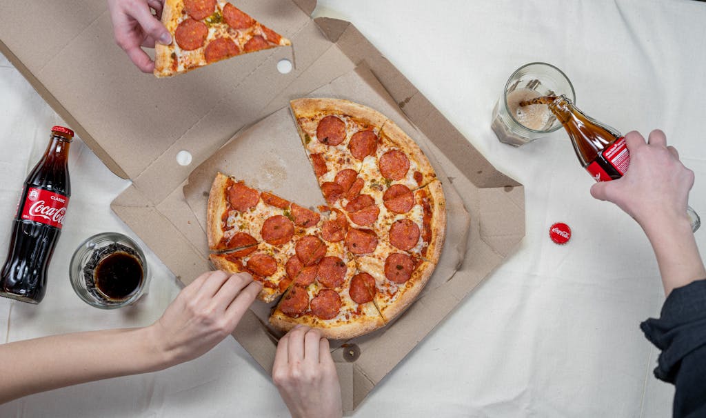 Top view of friends sharing pepperoni pizza and enjoying Coca Cola.