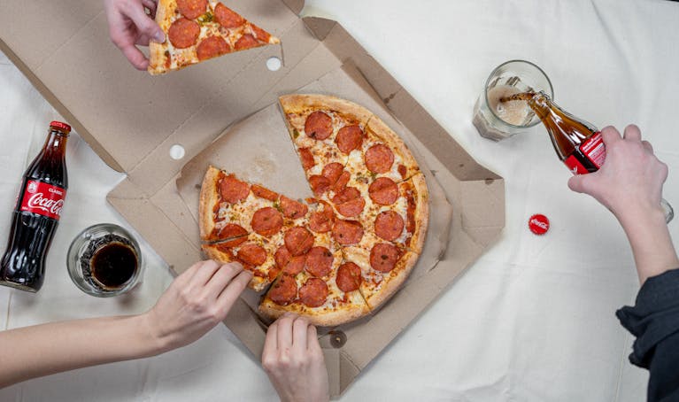Top view of friends sharing pepperoni pizza and enjoying Coca Cola.